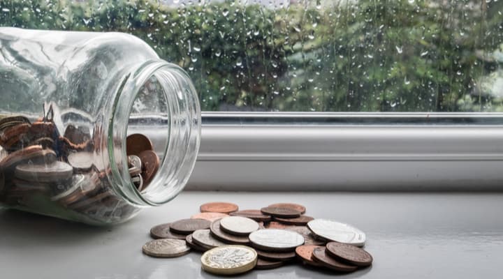 A jar of money tipped over with a rainy day in the background