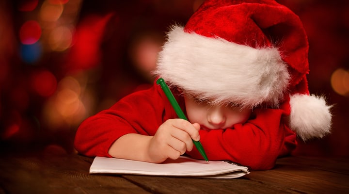 A child writing a Christmas list with a Santa hat on