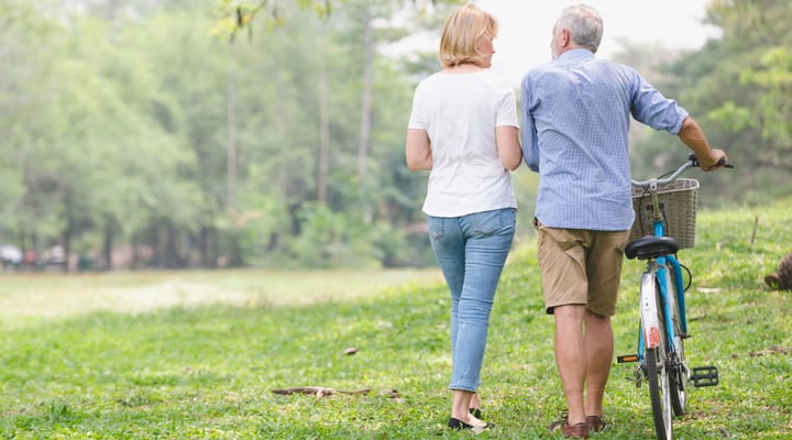 Senior couple walking through the park and pushing a bike