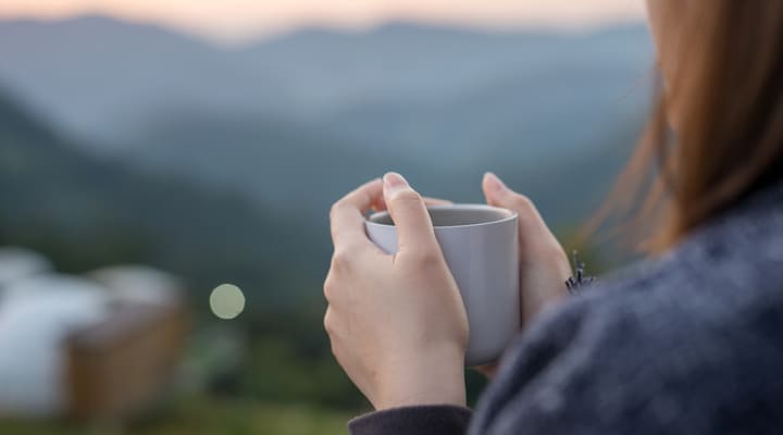 A woman holding a cup of coffee overlooking a green landscape