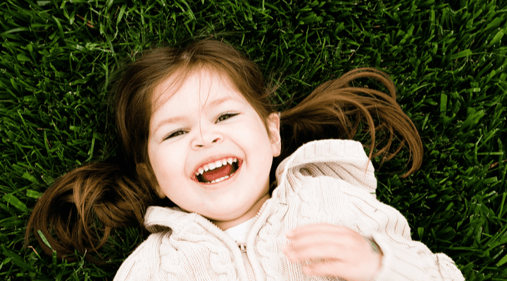 A child laughing as she lays on some grass