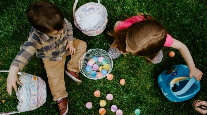 Two children sitting on some grass with Easter eggs and baskets.