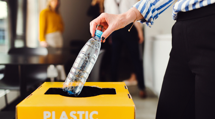 A woman putting a plastic bottle in a recycle bin.