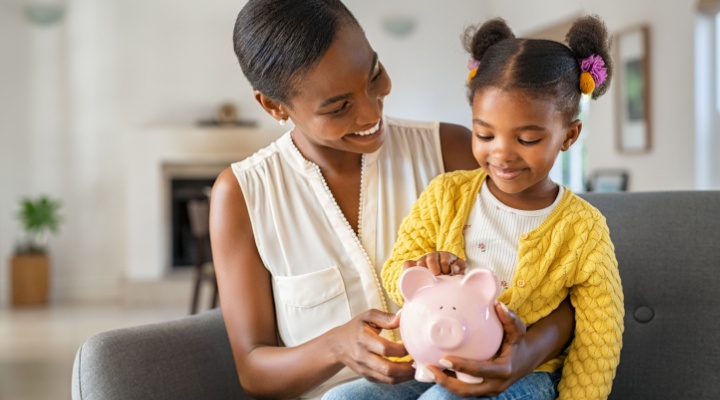 A woman with her child on her knee holding a piggy bank.