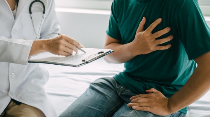 A man clutching his heart while a doctor examines him.