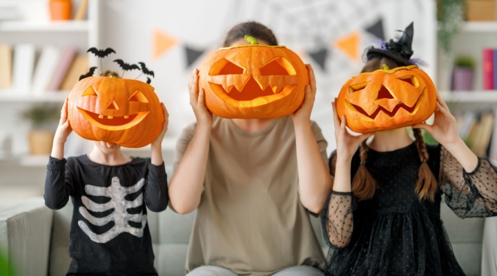 A mother and two children holding up carved pumpkins to their faces.