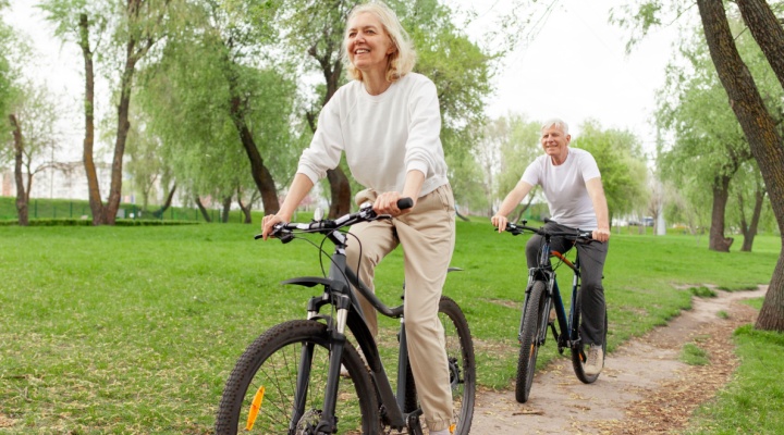 An elderly couple riding their bikes in the park.