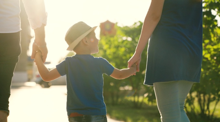 A family with a young child holding hands outdoors.